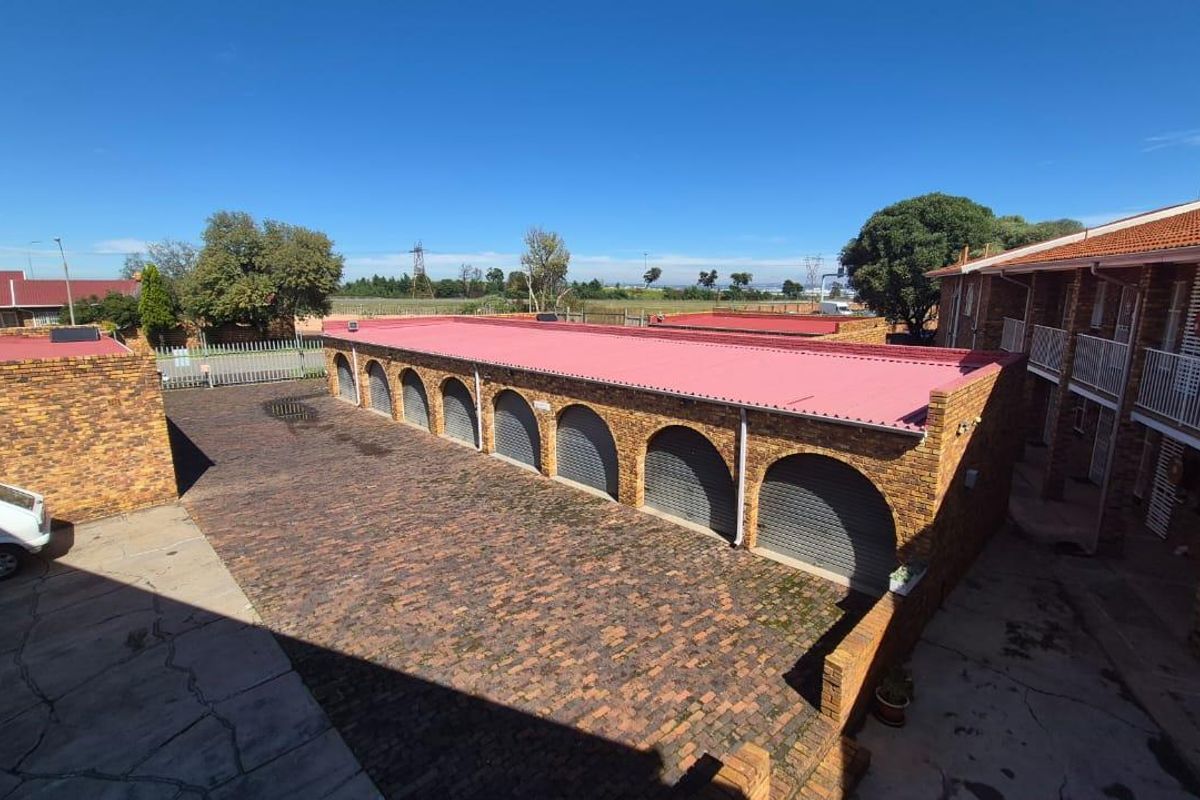 An elevated view of a townhouse complex courtyard featuring a row of arched brick garages with red metal roofing and paved driveway area.