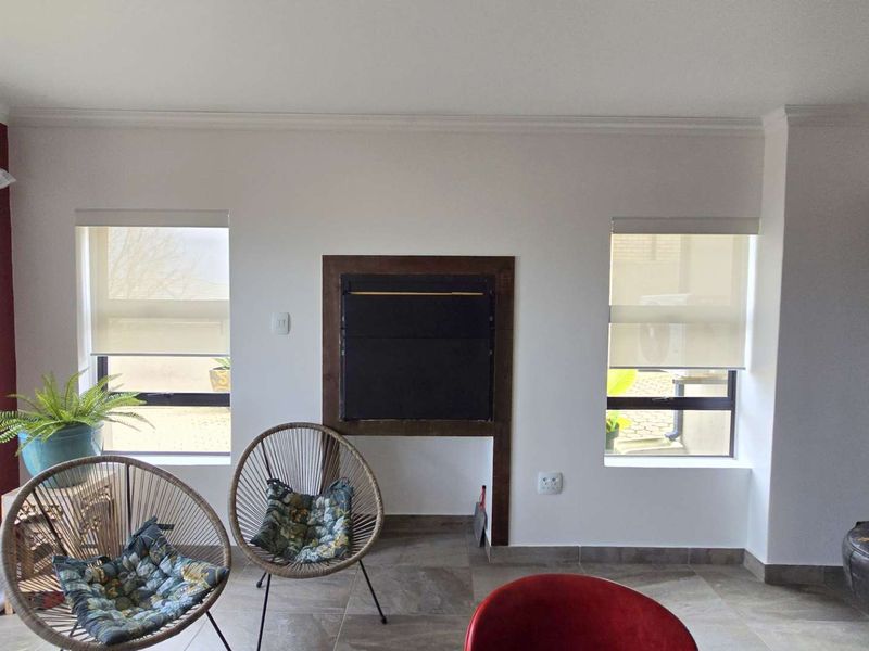 A bright living room featuring a central built-in fireplace, tiled flooring, and dual windows with fitted roller blinds.