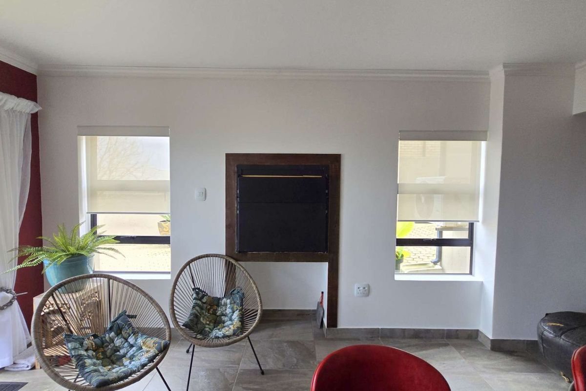 A bright living room featuring a central built-in fireplace, tiled flooring, and dual windows with fitted roller blinds.