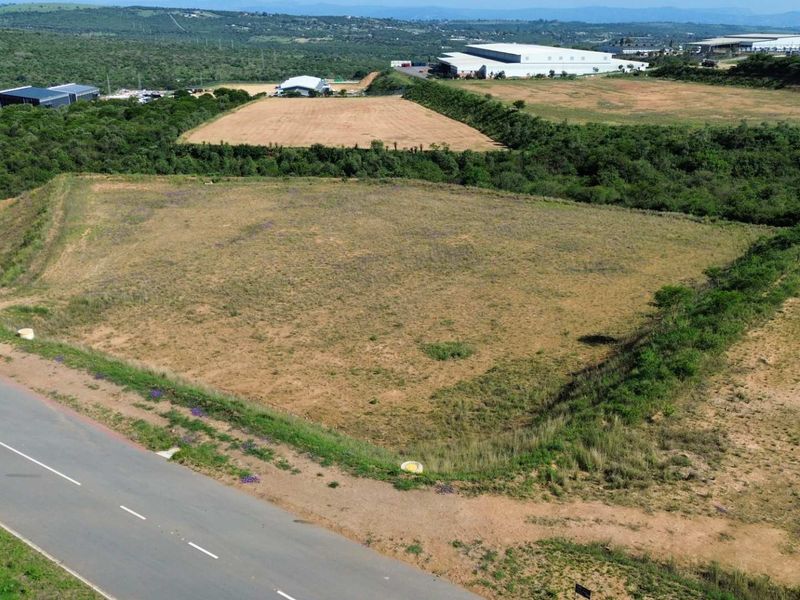 An aerial view of an undeveloped industrial land parcel with direct access to a paved road, situated in a developing industrial area.