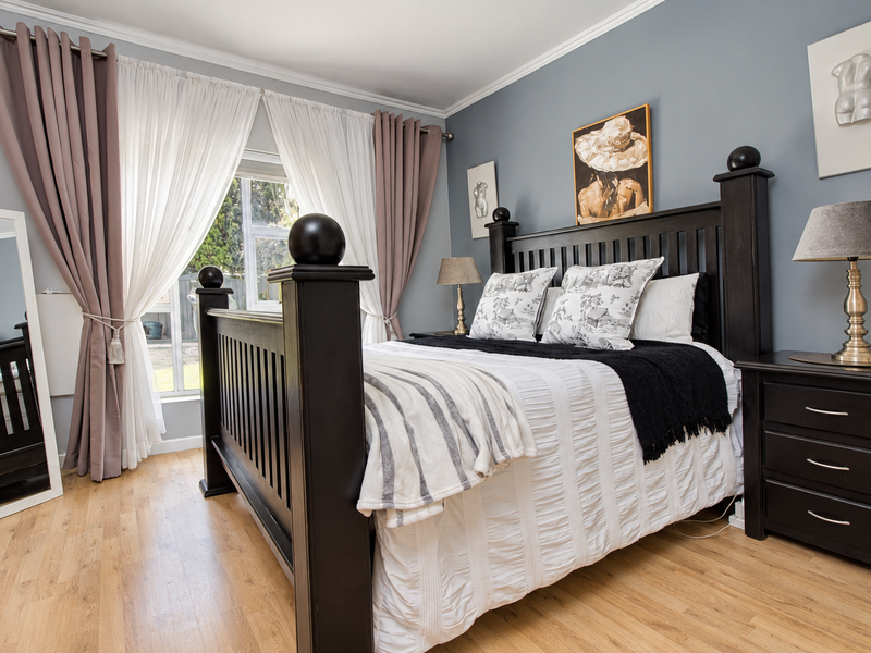 A well-maintained bedroom featuring light-toned laminate flooring, crown molding, and a large window allowing natural light into the space.