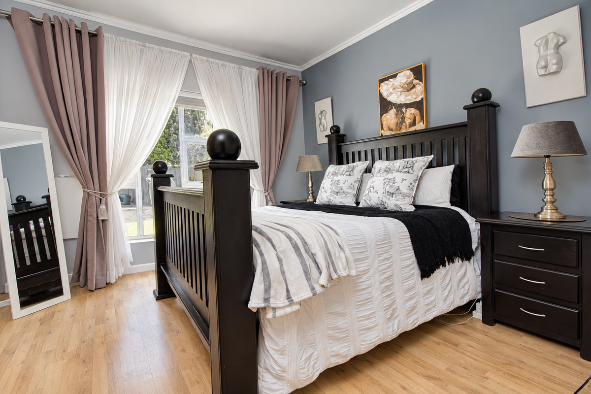 A well-maintained bedroom featuring light-toned laminate flooring, crown molding, and a large window allowing natural light into the space.