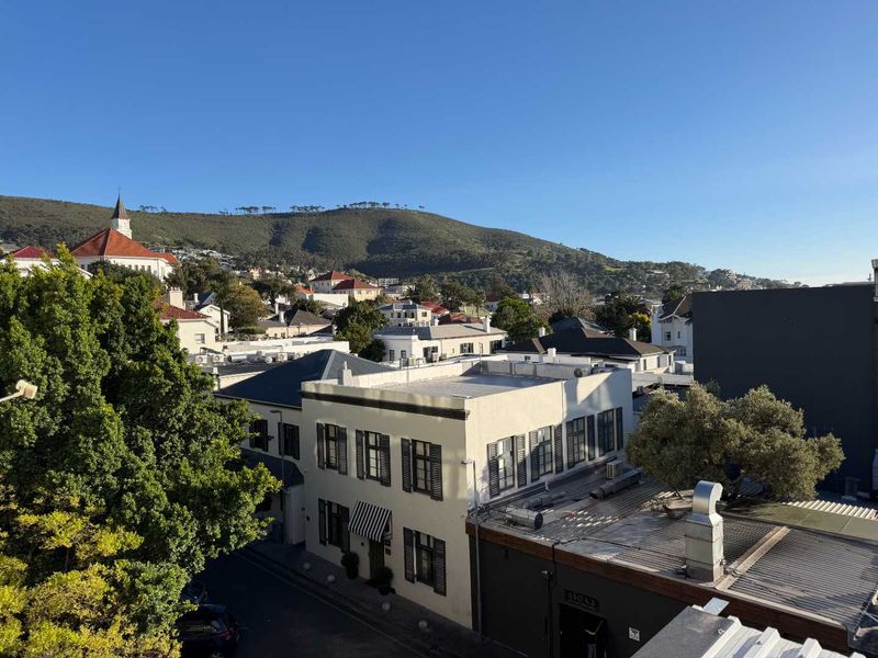 An elevated view overlooking the surrounding neighbourhood, streetscape, and distant mountain landscape under a clear blue sky.