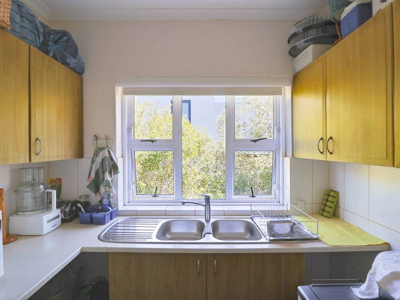 A functional scullery area featuring built-in wooden cabinetry, laminate countertops, and a double bowl stainless steel sink positioned beneath a window.
