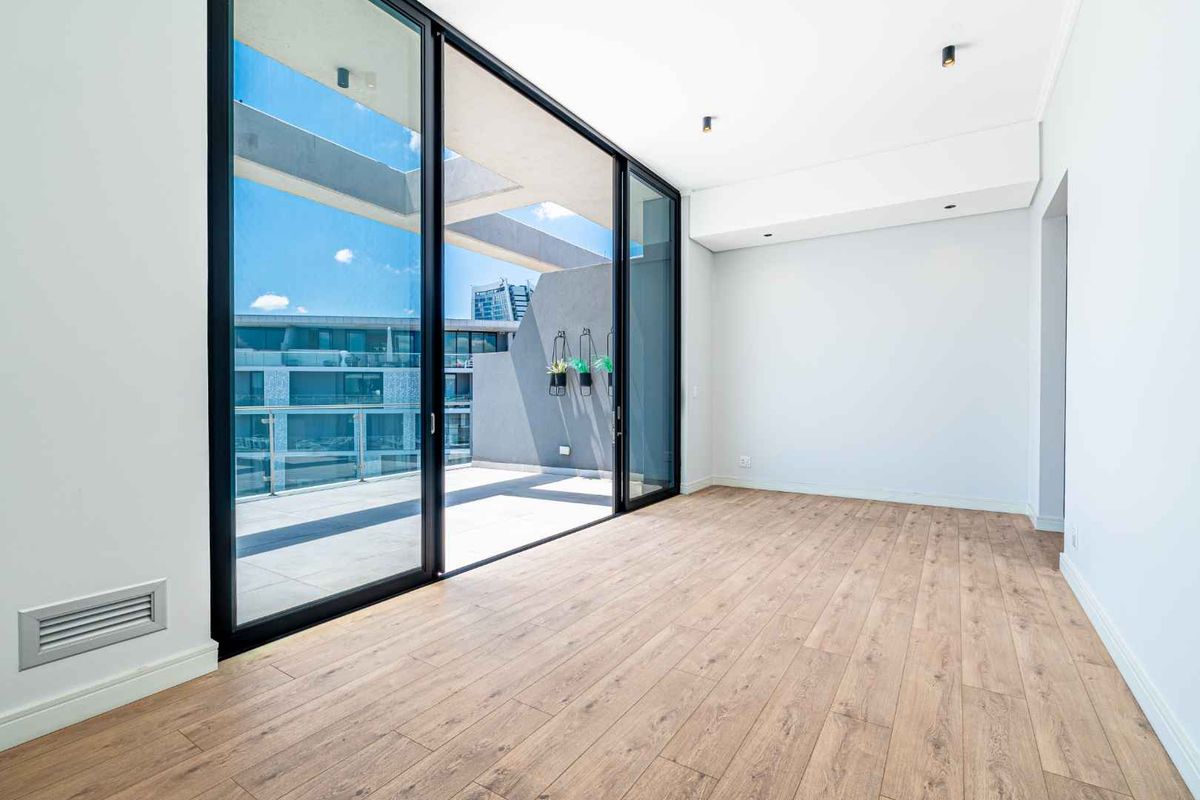 Bright and modern living area featuring light wood-look flooring, recessed ceiling lighting, and large sliding glass doors opening onto a spacious private balcony.