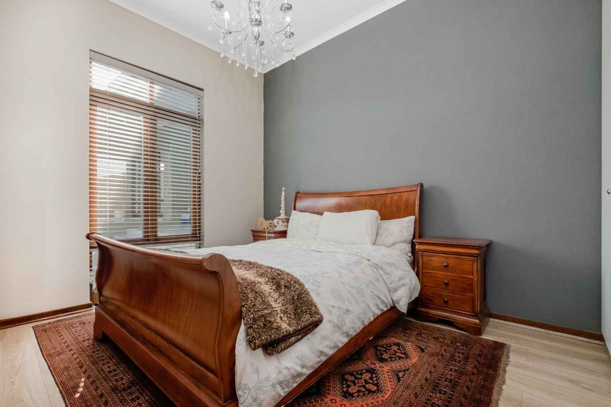 A well-maintained bedroom featuring laminate flooring, a feature wall, and a crystal chandelier, providing a comfortable and inviting sleeping space.