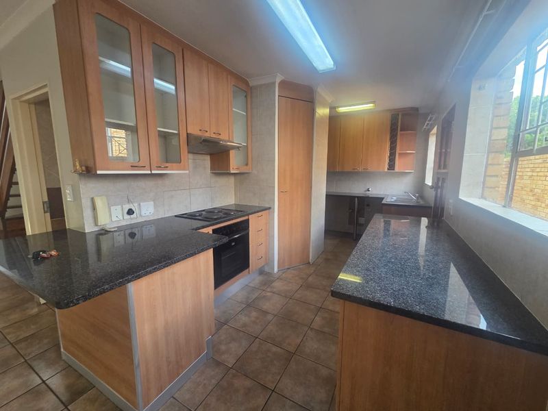 A functional kitchen featuring wooden cabinetry, granite countertops, built-in oven and hob, and tiled flooring, offering a practical layout for daily meal preparation.
