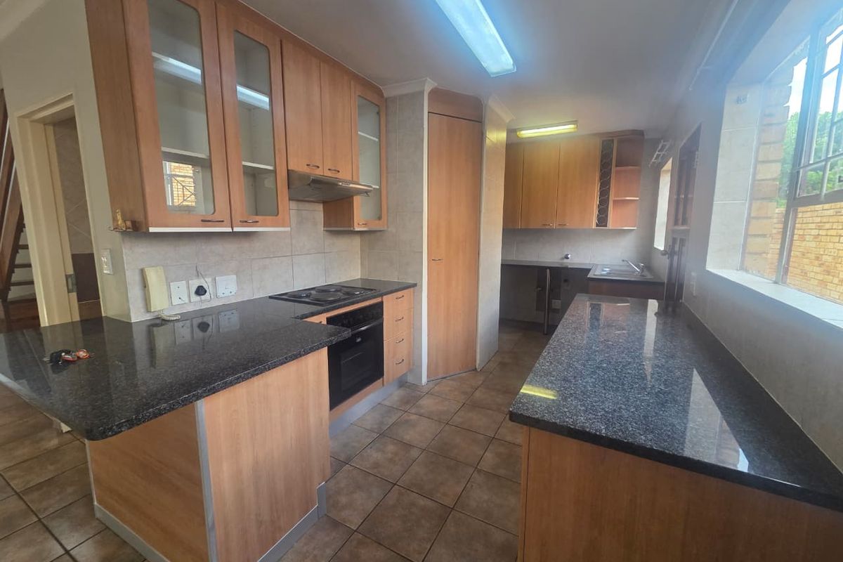 A functional kitchen featuring wooden cabinetry, granite countertops, built-in oven and hob, and tiled flooring, offering a practical layout for daily meal preparation.