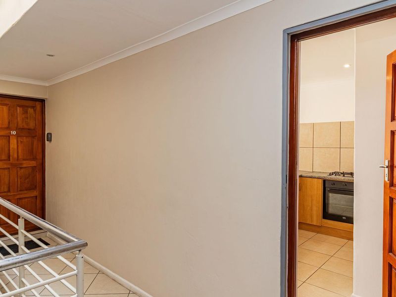 A clean, well-maintained apartment hallway featuring tiled floors, a metal balustrade, and wooden entrance doors leading to individual units.