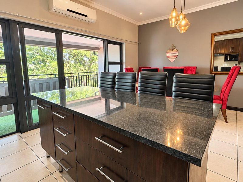 Open-plan living and kitchen area featuring a granite-topped island, tiled flooring, and large sliding doors leading to a balcony with natural light.