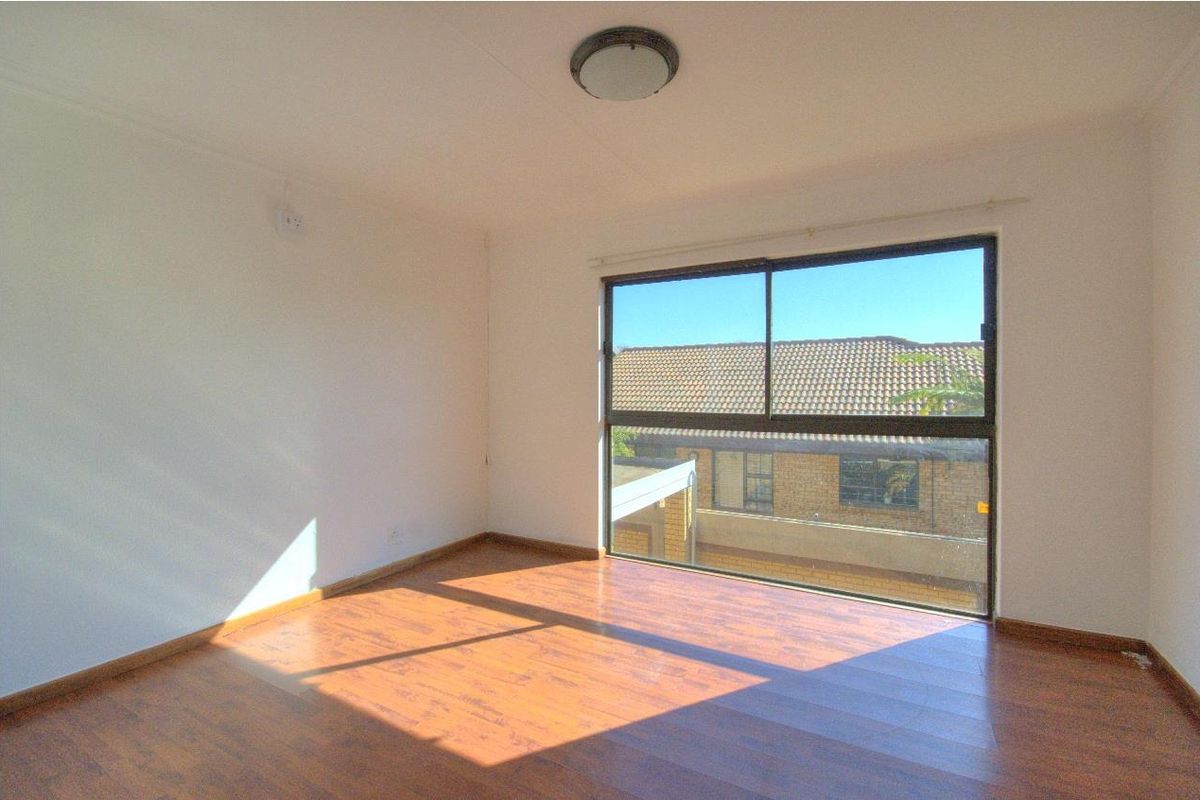 A bright, empty bedroom featuring laminate flooring and a large sliding window with natural light.