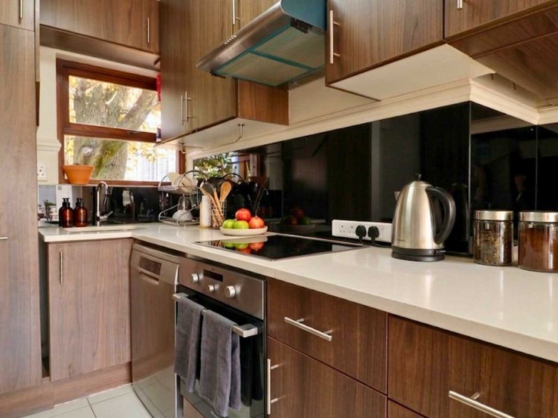 A modern kitchen featuring wood-finish cabinetry, stone countertops, a glass splashback, and integrated appliances including an oven, hob, and dishwasher.