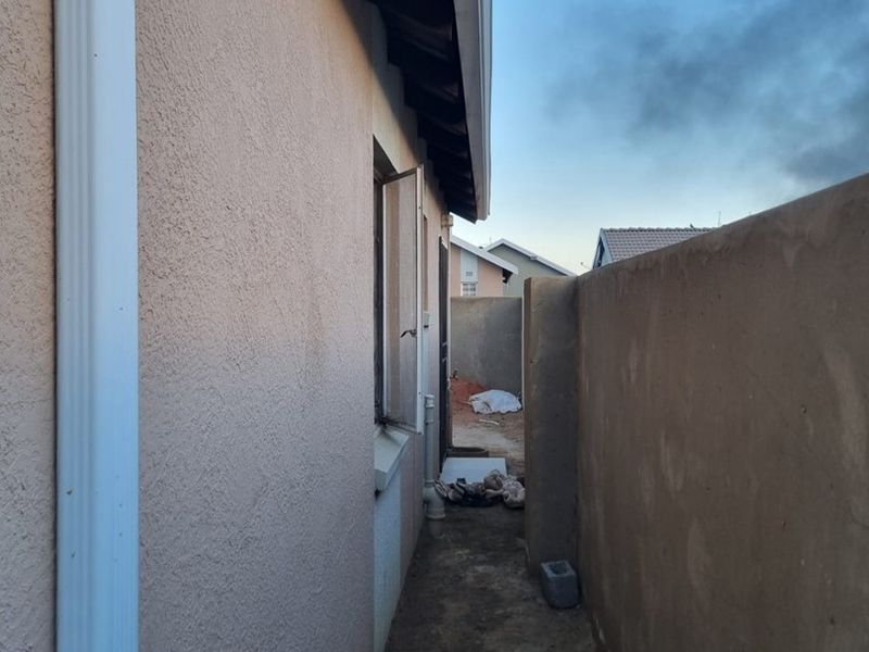 A narrow side passage of the property featuring a boundary wall, downpipe, and unfinished ground surface.