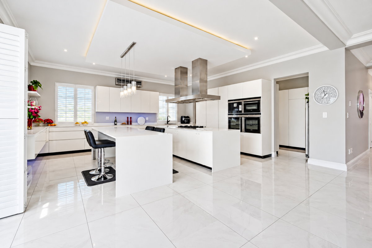 Modern, high-end kitchen featuring a large central island, integrated stainless steel appliances, sleek white cabinetry, and polished porcelain flooring with recessed ceiling lighting.