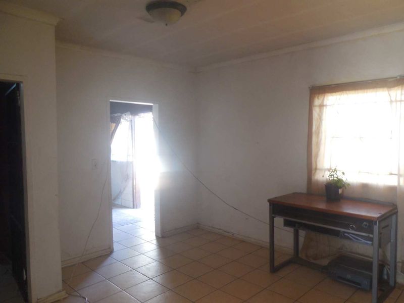 A vacant living room featuring tiled flooring and a ceiling light fixture, requiring cosmetic updates and repairs to wall finishes.