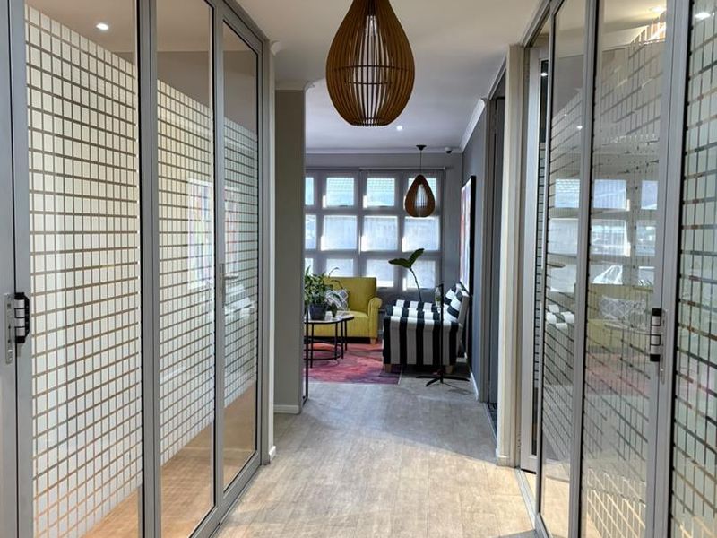 A modern office hallway featuring glass partition walls with frosted privacy detailing and wood-look laminate flooring, leading into an open-plan workspace.