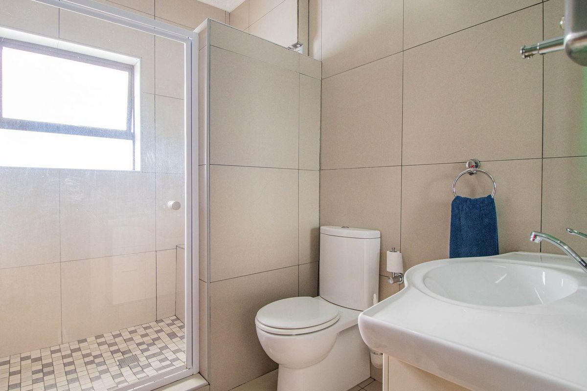 A modern bathroom featuring a glass-enclosed shower, a white ceramic toilet, and a vanity basin with wall-mounted fixtures and neutral tiling.