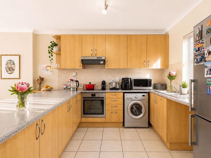A functional U-shaped kitchen featuring light wood-finish cabinetry, laminate countertops, tiled backsplash, and integrated appliances including an oven and extractor fan.