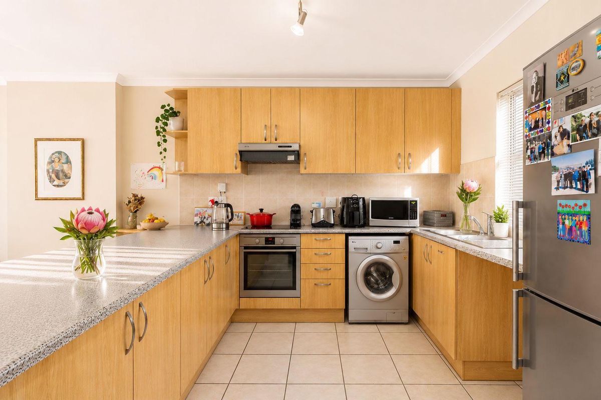 A functional U-shaped kitchen featuring light wood-finish cabinetry, laminate countertops, tiled backsplash, and integrated appliances including an oven and extractor fan.