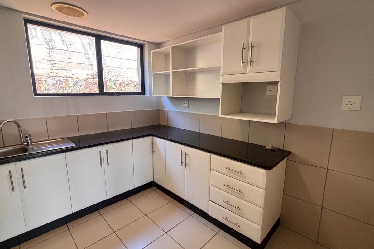 A clean, functional kitchen featuring white built-in cabinetry, dark granite countertops, a stainless steel sink, and neutral tiled finishes.