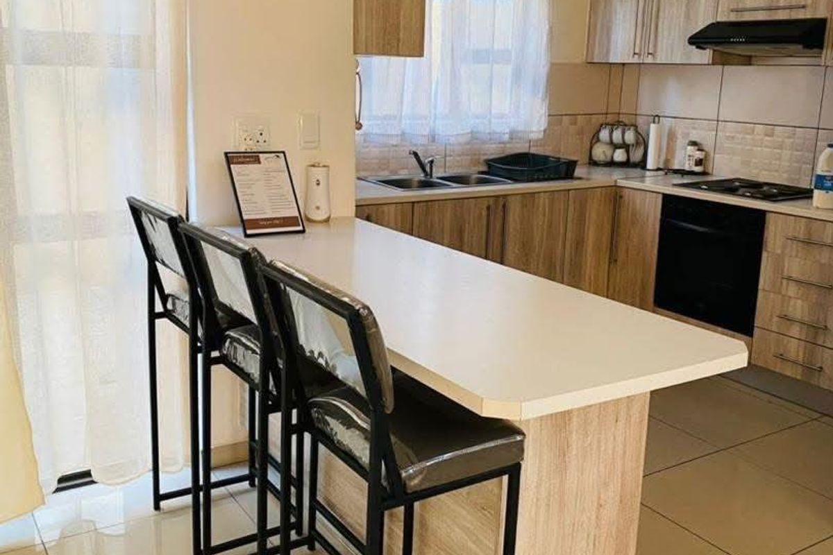 Modern kitchen featuring light wood-finish cabinetry, built-in oven, hob, extractor fan, and a functional breakfast bar with tiled flooring throughout.