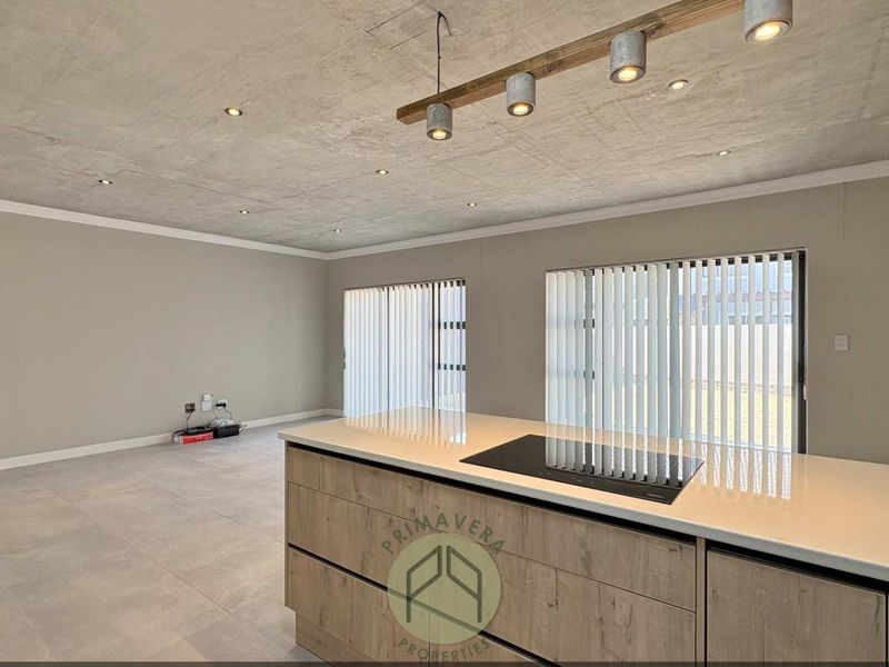 Modern open-plan living area featuring an exposed concrete ceiling, tiled floors, and a contemporary kitchen island with a built-in induction cooktop.