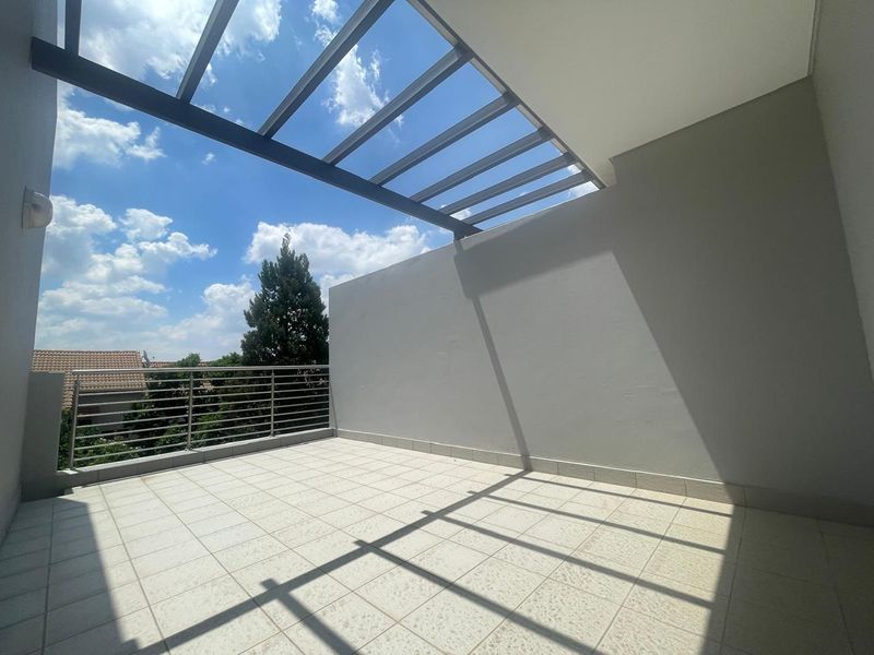 A spacious, open-air balcony featuring a modern metal pergola, tiled flooring, and a secure metal balustrade with clear views.