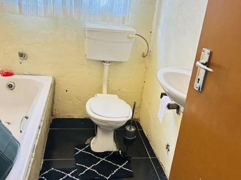 A compact bathroom featuring a bathtub, toilet, and wall-mounted basin with dark floor tiles and dated wall finishes.