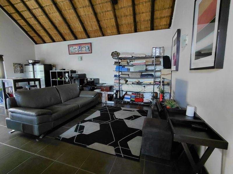 Spacious living area featuring a high vaulted ceiling with exposed timber rafters and traditional thatch roofing, complemented by durable tiled flooring.