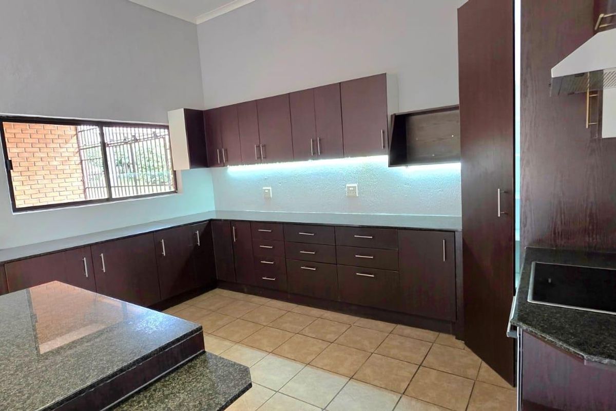 A modern kitchen featuring dark wood cabinetry, granite countertops, a built-in hob, and an extractor fan, complemented by tiled flooring and under-cabinet lighting.
