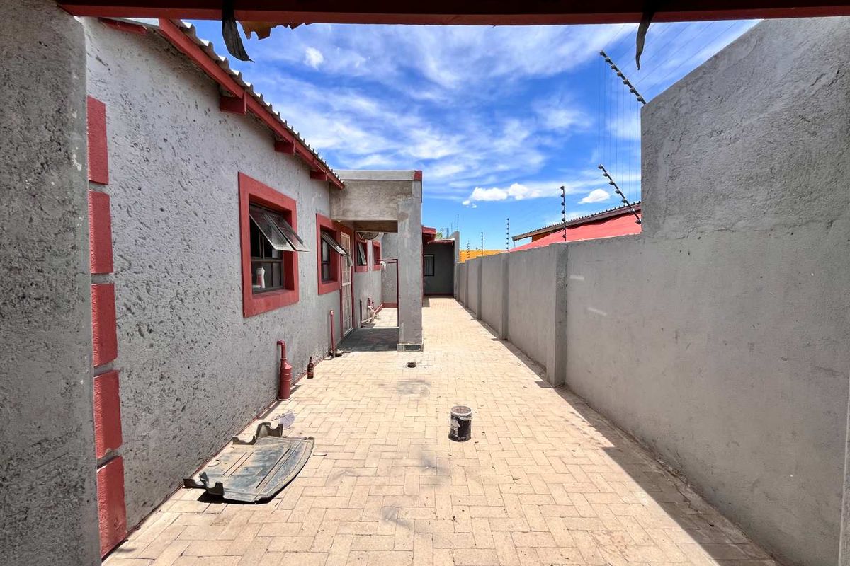 A paved side walkway or courtyard area featuring high perimeter walls with electric fencing and direct access to the main building structure.