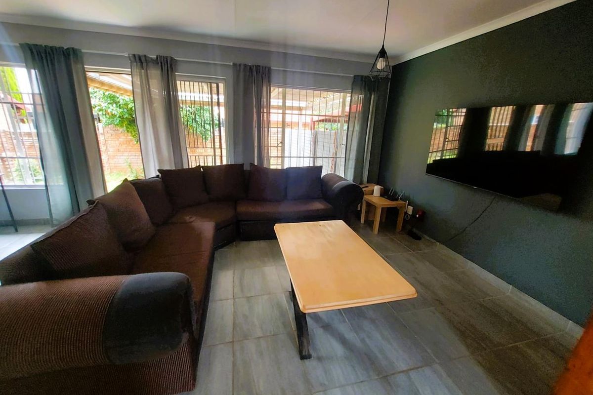 A comfortable living room featuring large windows, tiled flooring, and a dark accent wall, providing a functional space for relaxation.
