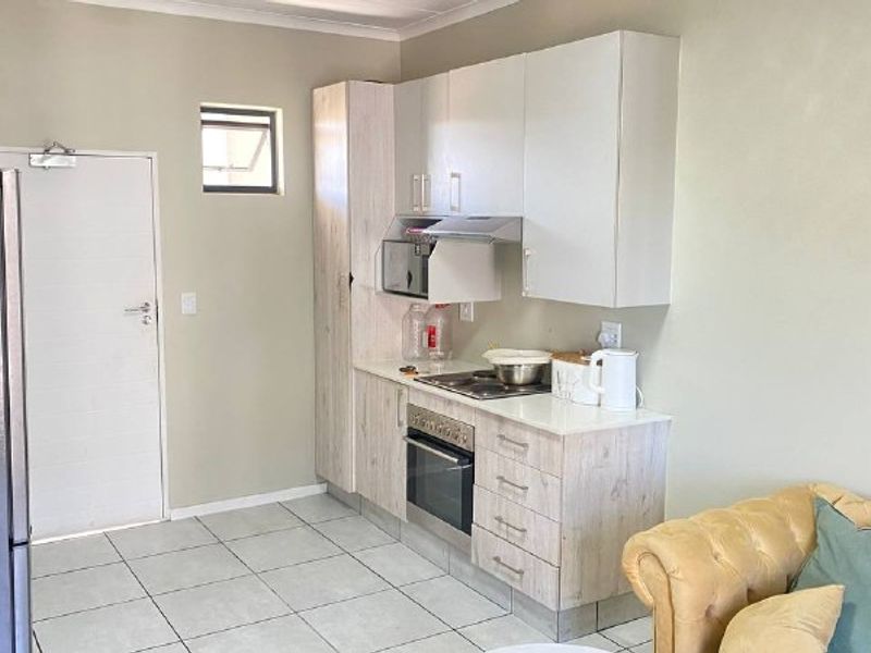 Open plan kitchen area featuring light wood-look cabinetry, built-in oven and hob, extractor fan, and neutral tiled flooring.