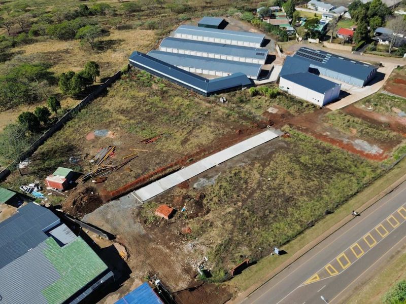 Aerial view of a commercial property featuring multiple metal-roofed warehouse structures, a concrete driveway, and significant undeveloped land area.