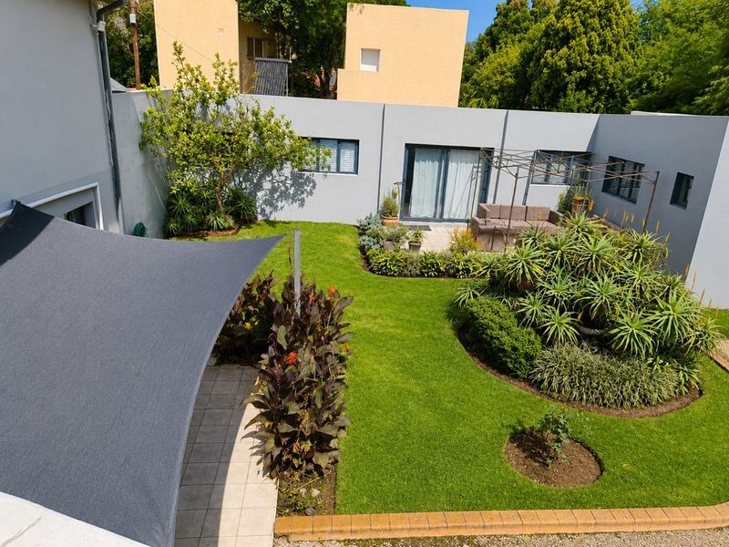 A well-maintained rear garden featuring a manicured lawn, established landscaping, a tiled patio area with a shade sail, and secure perimeter walling.