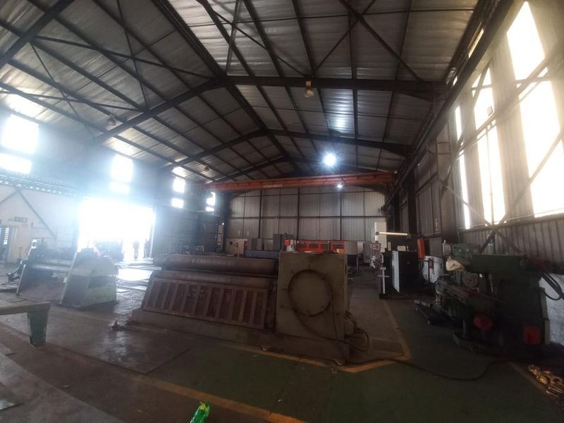 Spacious industrial warehouse featuring a high steel truss roof, overhead crane system, and durable concrete flooring, suitable for heavy manufacturing or storage operations.