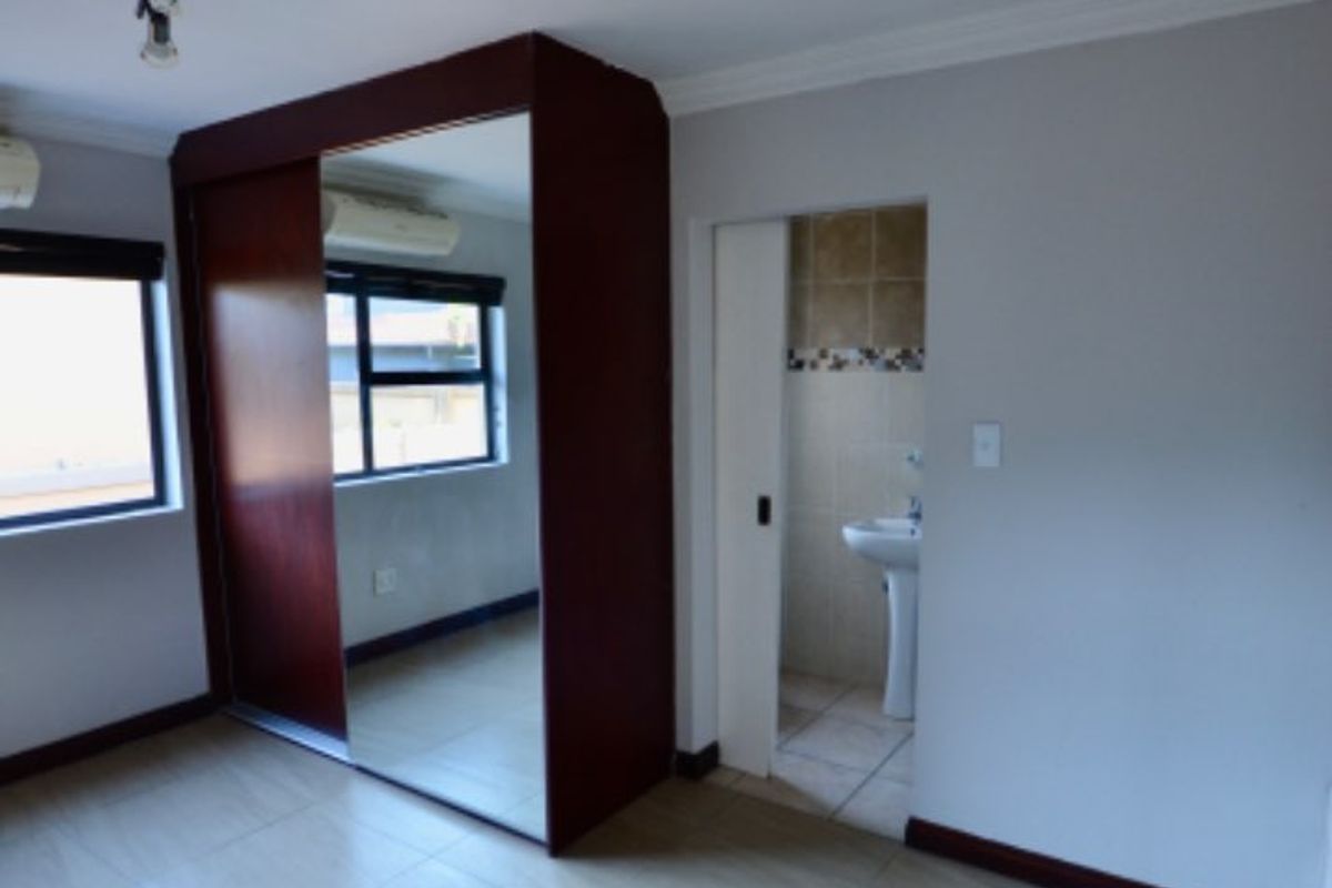 A spacious bedroom featuring tiled flooring, a large built-in wardrobe with mirrored sliding doors, and direct access to an en-suite bathroom.