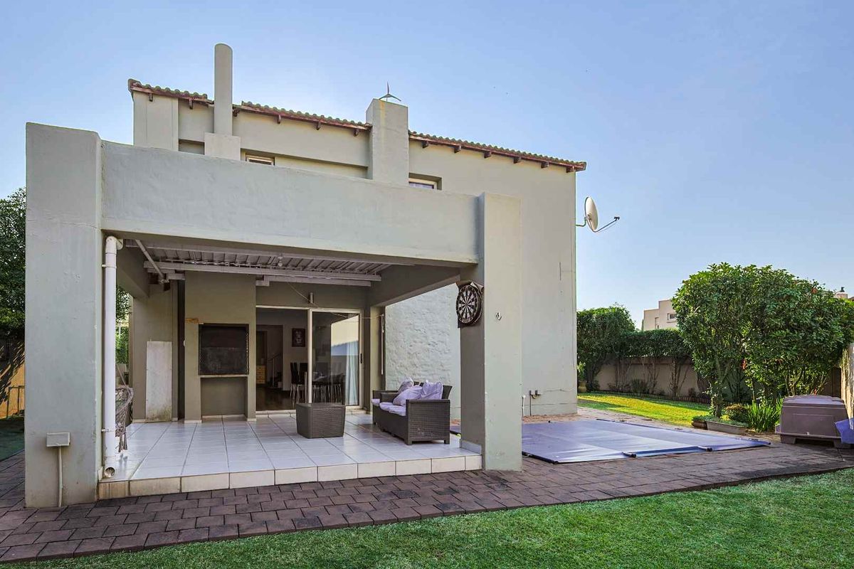 Rear view of the property featuring a covered patio with a built-in braai, paved outdoor area, and a swimming pool with a cover.