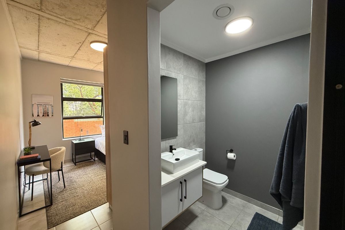 Modern bathroom featuring a vessel sink on a vanity cabinet, tiled flooring, and neutral grey wall finishes, adjacent to a bedroom area.