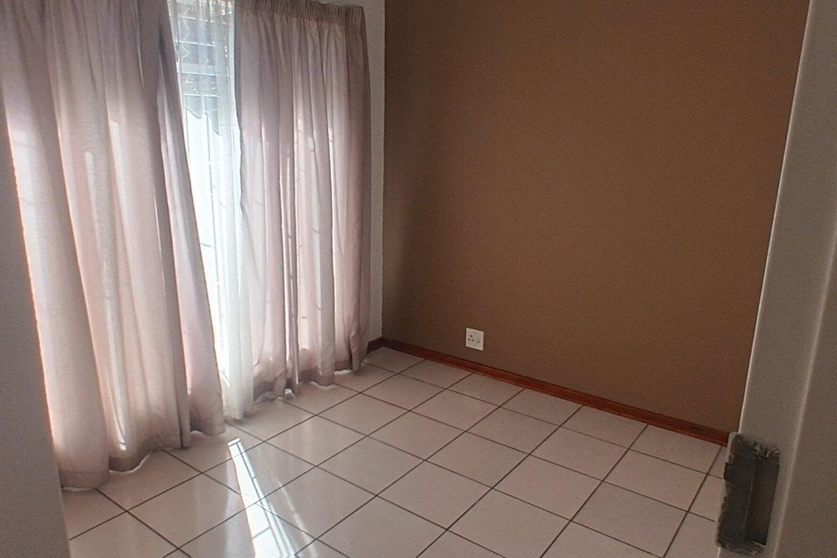 A vacant bedroom featuring neutral tiled flooring and a brown accent wall, offering a clean and simple space ready for personalization.
