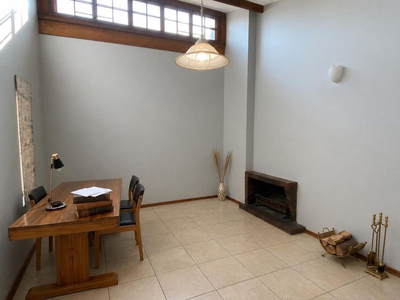 A spacious living area featuring high ceilings with clerestory windows, tiled flooring, and a traditional brick fireplace.
