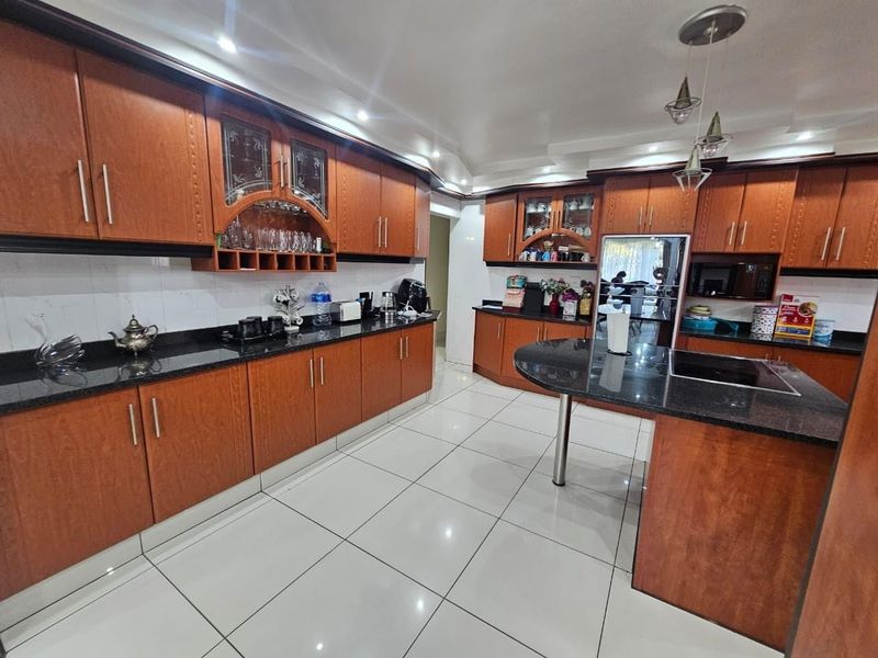 Spacious kitchen featuring dark wood cabinetry, granite countertops, integrated appliances, and polished ceramic floor tiles.