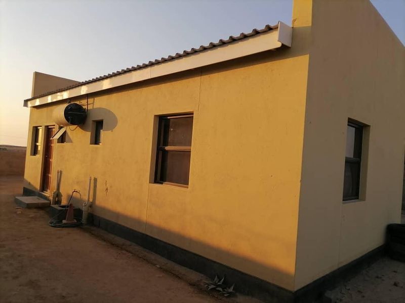 Rear view of a single-story residential property featuring plastered walls, metal roof sheeting, and a mounted solar geyser unit.