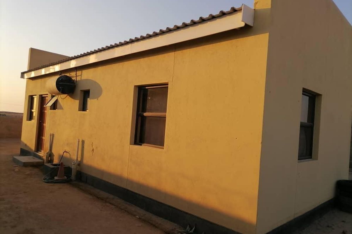 Rear view of a single-story residential property featuring plastered walls, metal roof sheeting, and a mounted solar geyser unit.