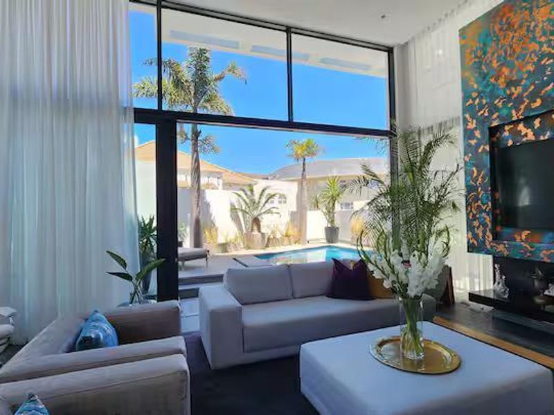 Modern living room featuring expansive floor-to-ceiling windows, a striking custom media wall, and seamless indoor-outdoor flow to the pool area.