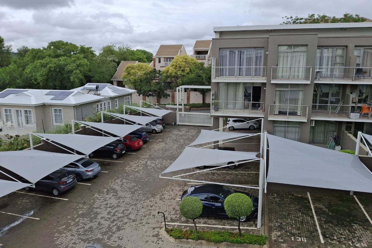 Aerial view of an apartment complex parking area featuring paved bays with shade sail structures and multi-story residential units with balconies.