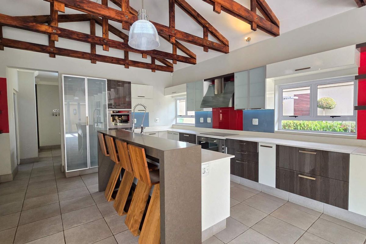 Modern kitchen featuring exposed timber roof trusses, a central island with stone countertops, built-in appliances, and contemporary cabinetry with vibrant red accents.