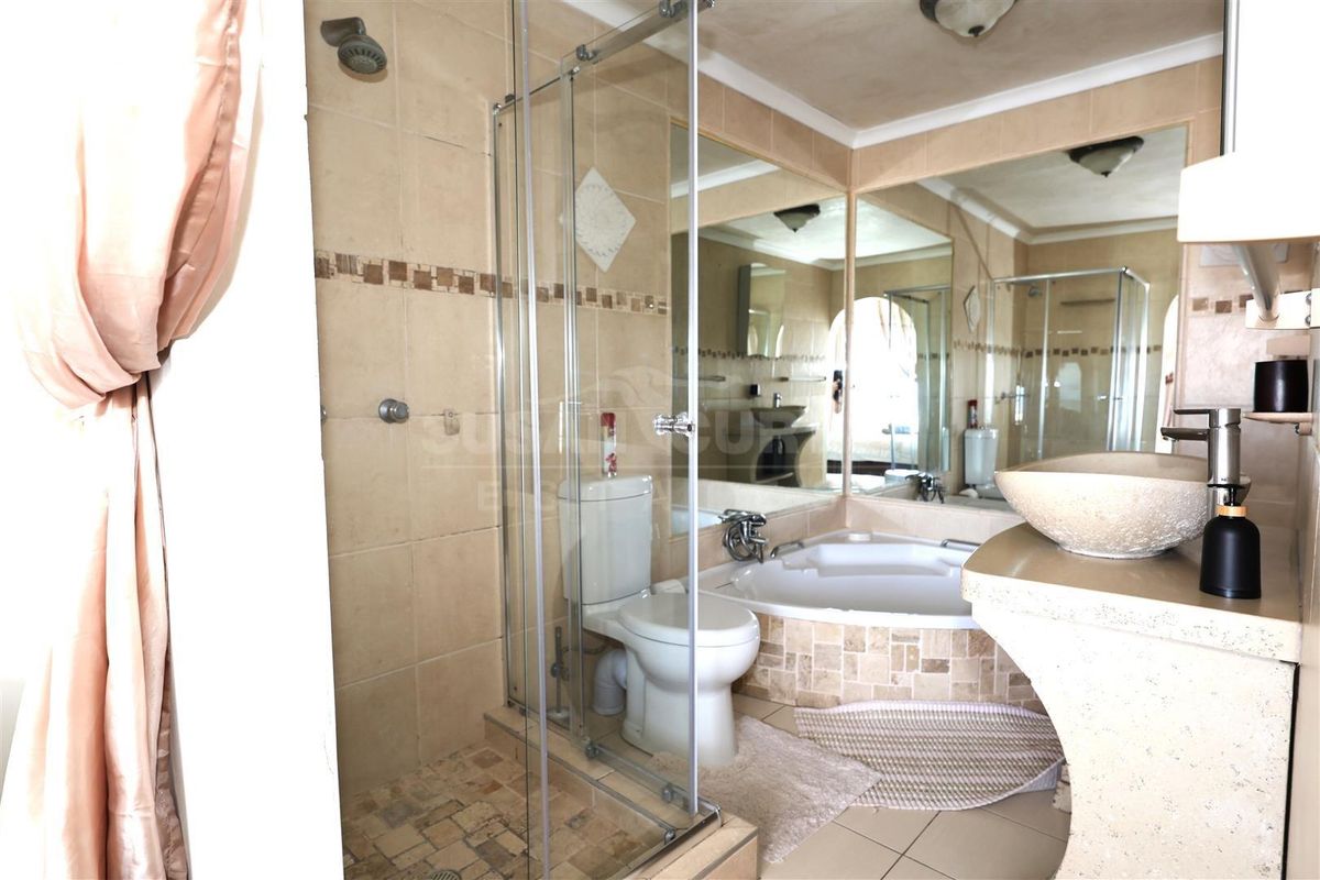 A functional bathroom featuring a glass-enclosed shower, a corner soaking tub, and a stone-style vanity basin with large wall-mounted mirrors.