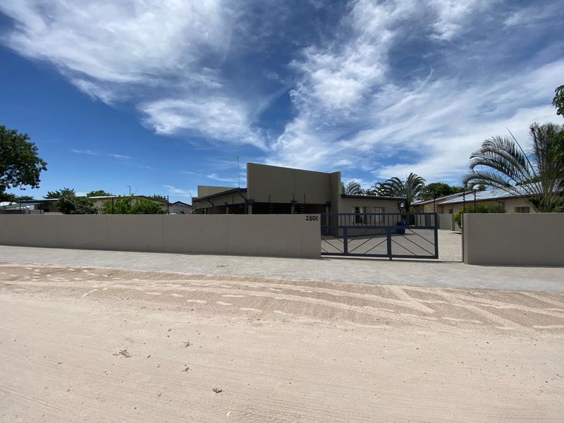 Front exterior view of the property featuring a secure perimeter wall, metal driveway gate, and electric fencing.