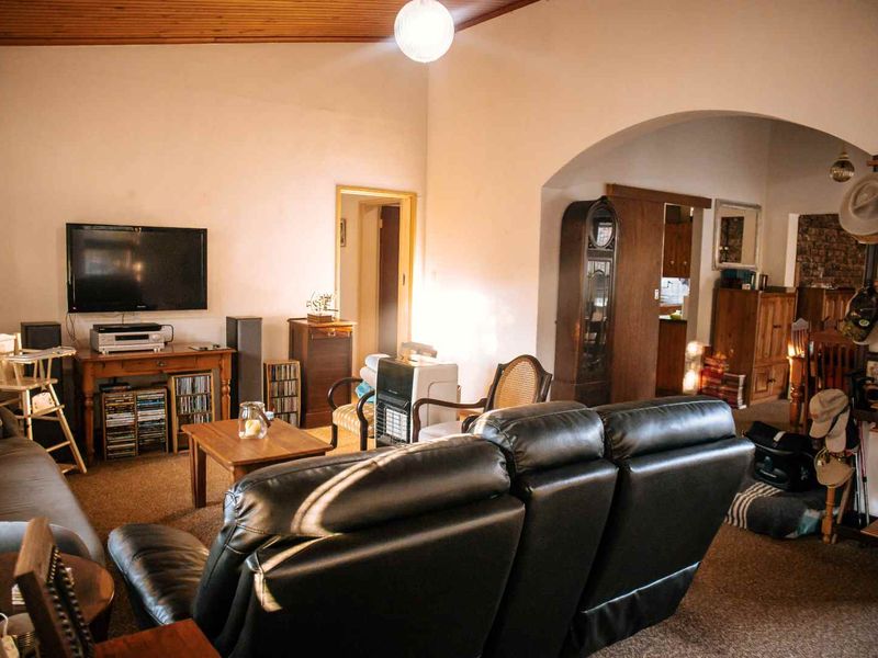 A living room featuring a vaulted timber-clad ceiling, carpeted flooring, and an arched entryway leading to an adjacent space.